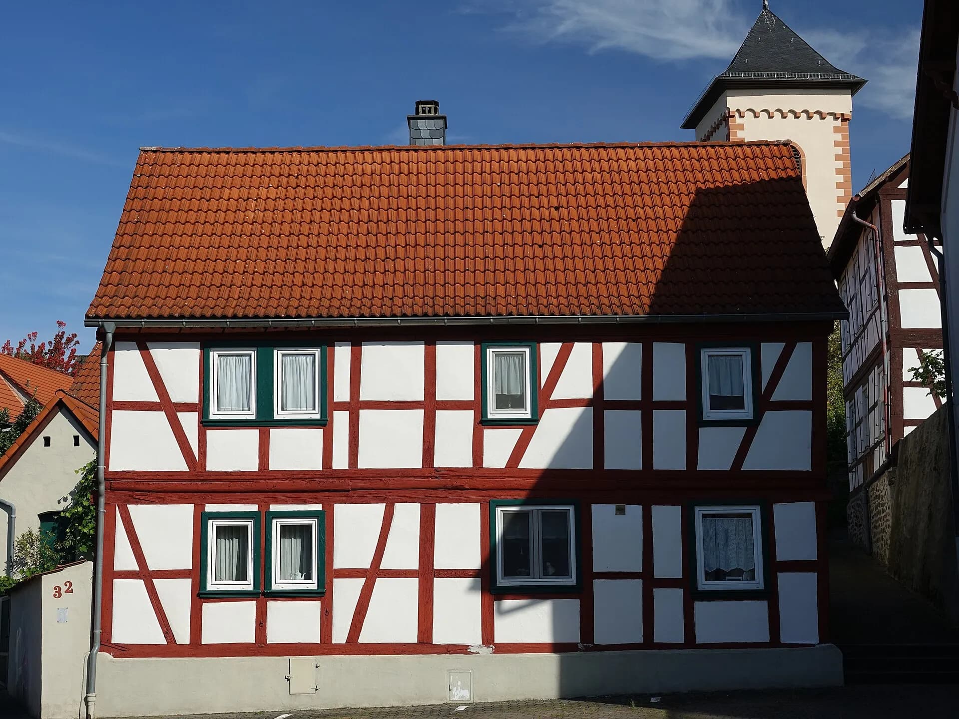Rot-weißes Fachwerkhaus mit Wehrturm im Hintergrund an der Alten Rathausstraße in Hanau-Mittelbuchen