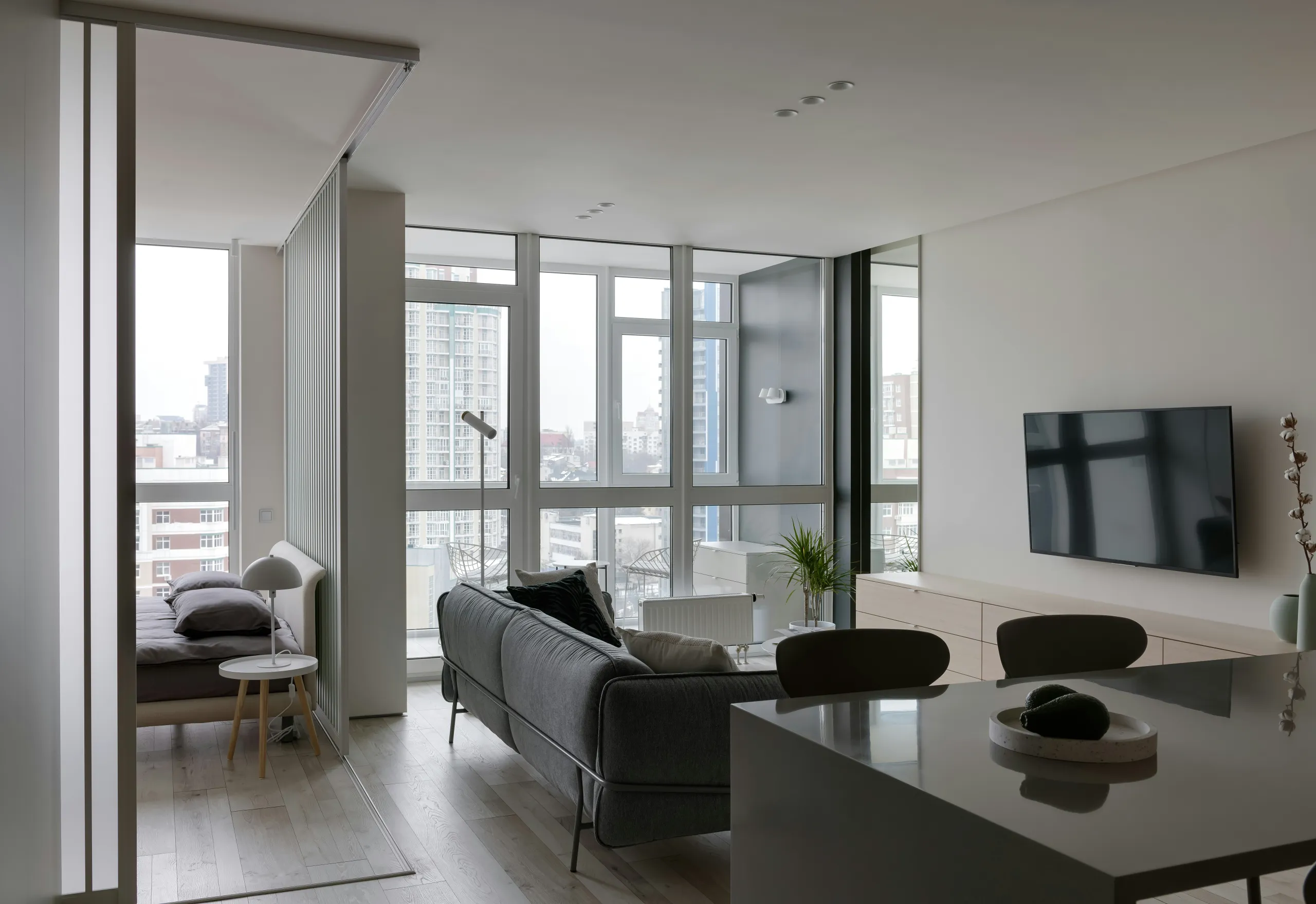 Apartment mit grauem Sofa, Schlafbereich hinter Glaswand und Stadtblick