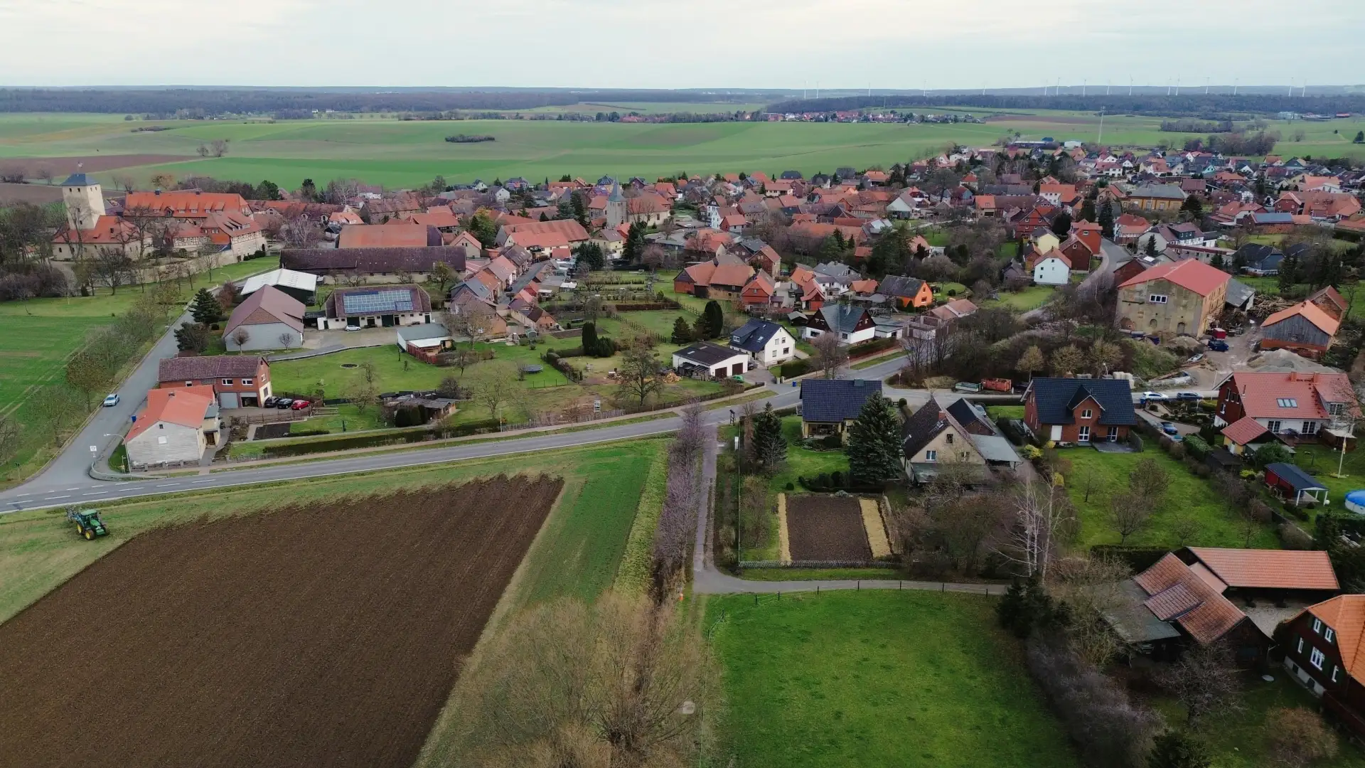 Luftbild eines Dorfs mit Burgturm, Äckern und Wiesen am Ortsrand