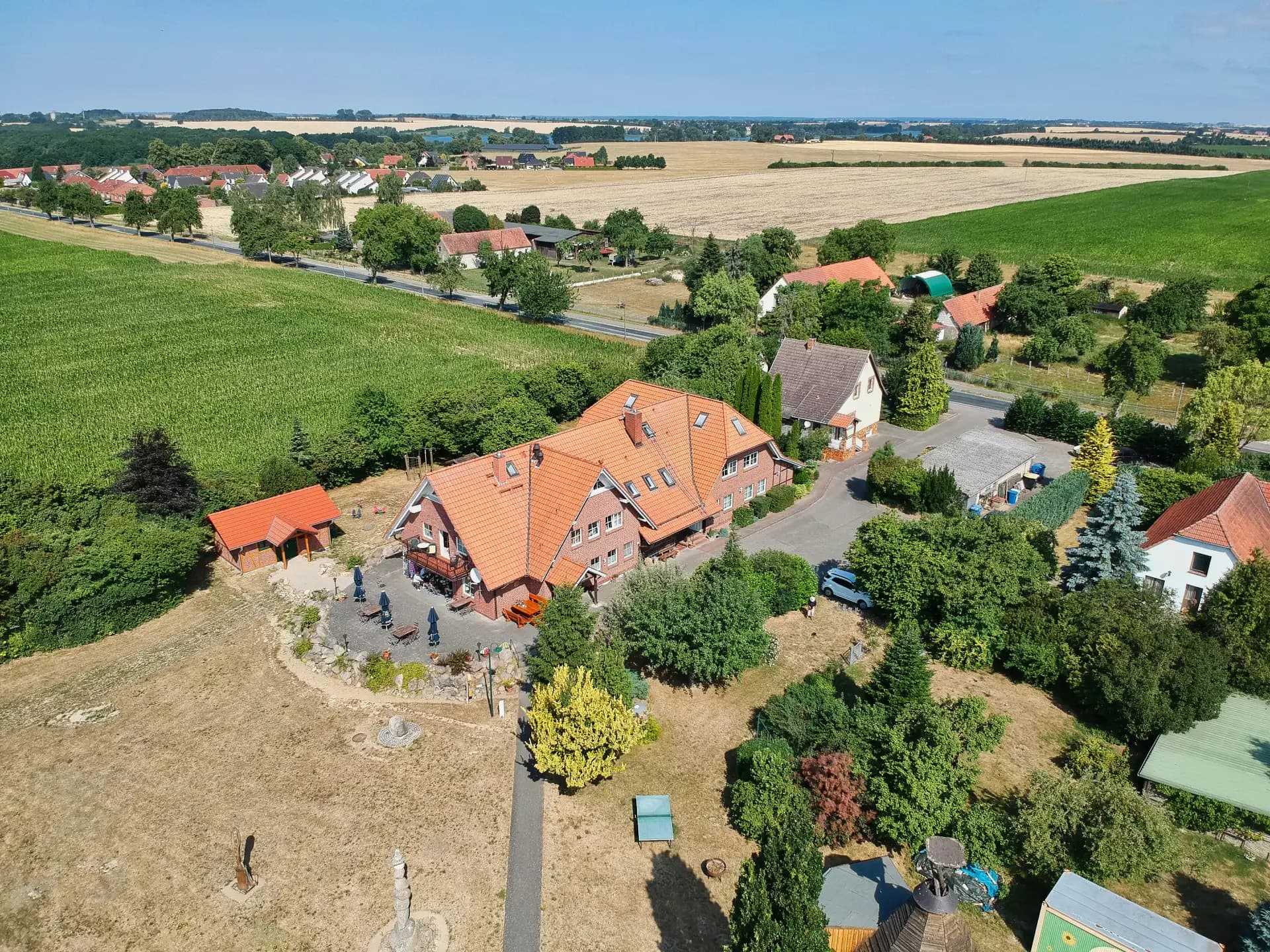 Luftbild eines Dorfrands mit roten Dächern, Feldern und Seen